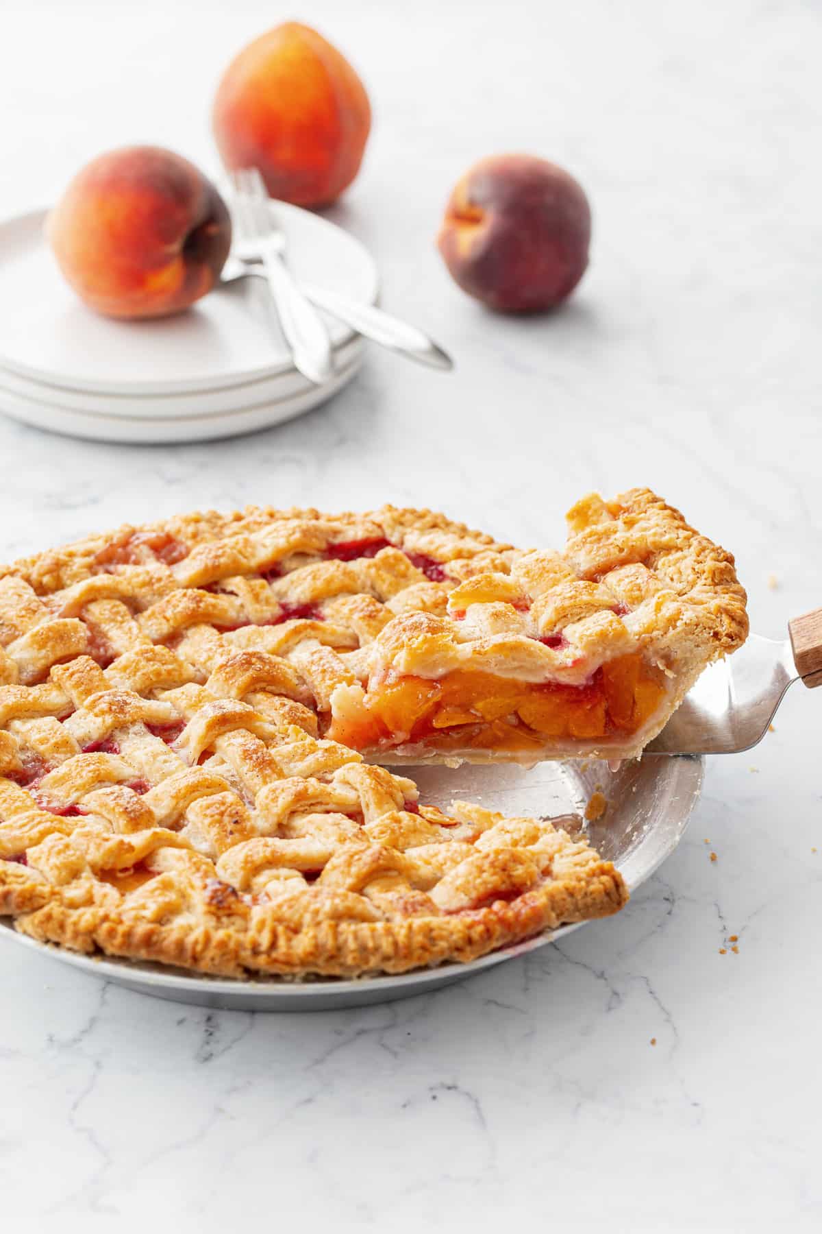 Cut slice of Vanilla Bean Peach Pie lifting out of the pan with a pie server, pie is topped with a lattice crust.