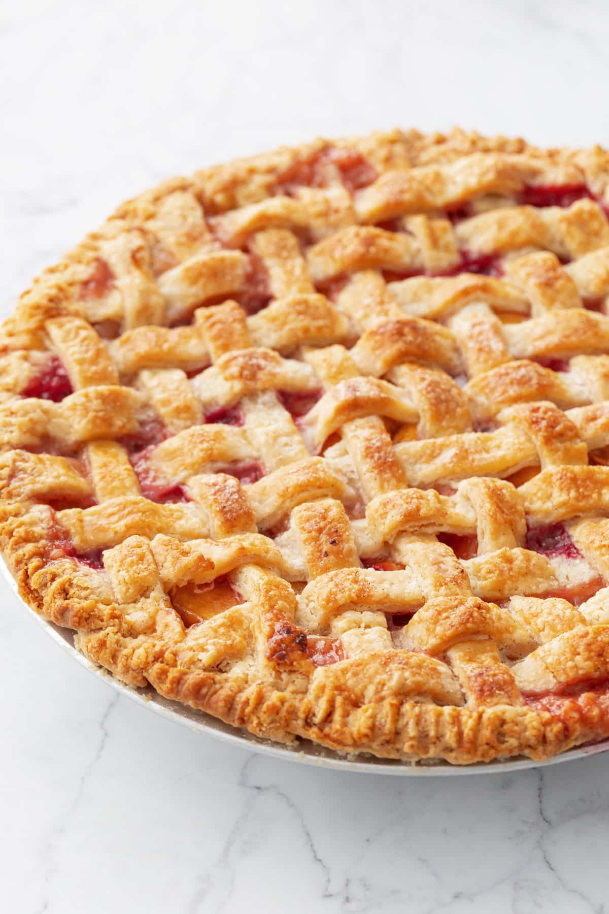 Lattice topped peach pie sitting on a marble background.