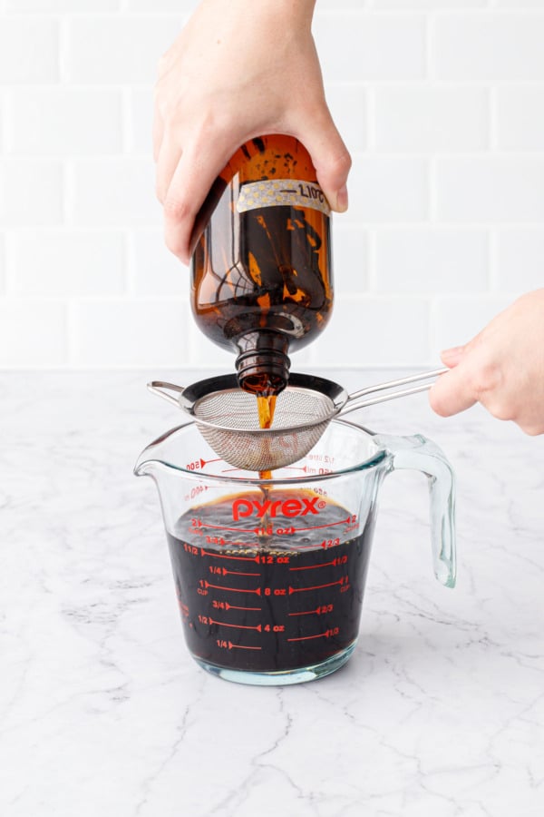 Straining the final vanilla extract through a fine mesh sieve into a glass measuring cup.