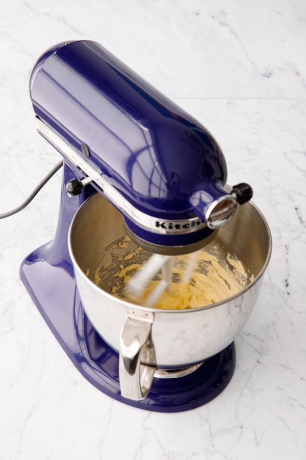 Butter being creamed in a blue stand mixer fitted with the paddle attachment.