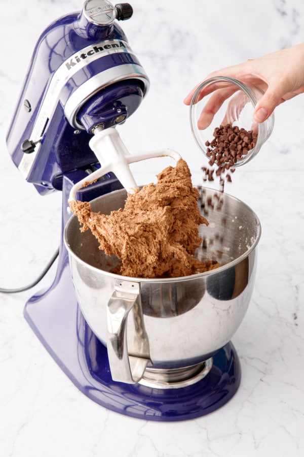 Pouring mini chocolate chips into mixing bowl with Nutella cookie dough.