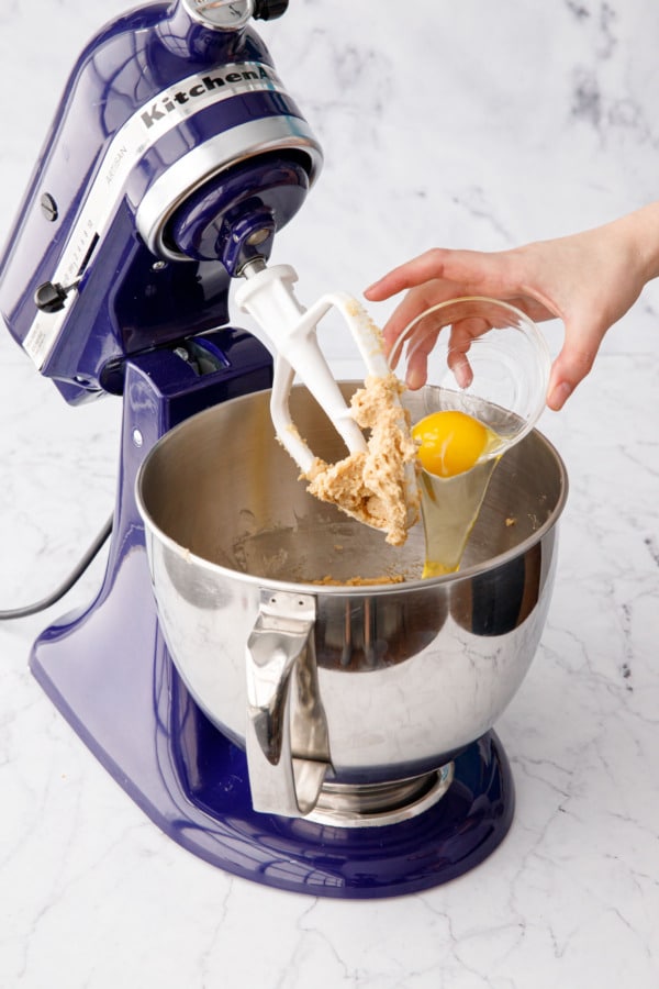 Adding egg to mixing bowl with creamed butter and sugar.