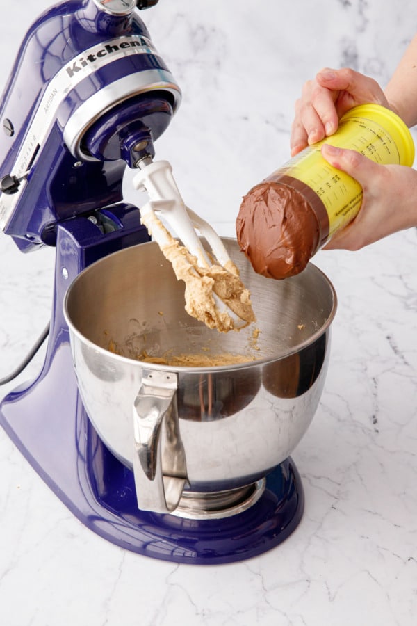A plunger measuring cup pouring nutella into mixing bowl with the rest of the dough.