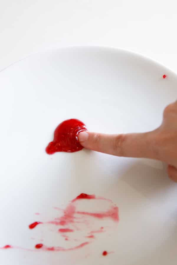 Finger nudging through chilled jam to check for doneness; it wrinkles up slightly behind the fingertip to indicate a proper set.