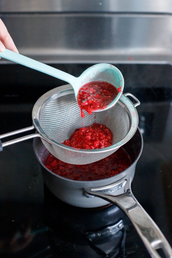 Silicone ladle pouring some of the softened raspberries into a fine mesh sieve.