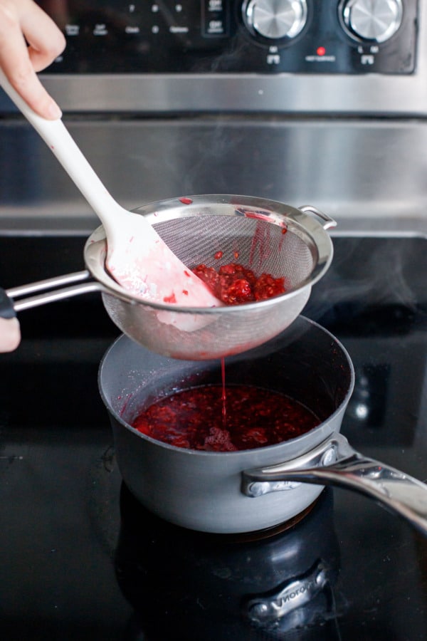 Pressing raspberries through a fine mesh sieve using a spatula.