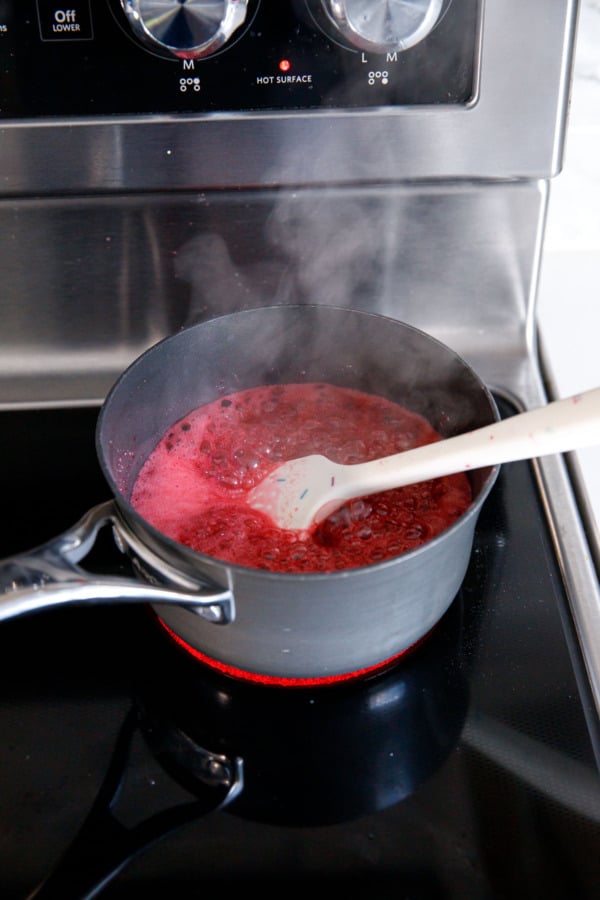 Raspberry jam simmering and bubbling up on the stovetop with a spatula.