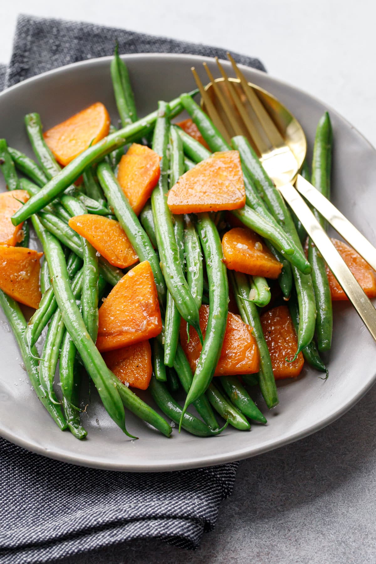 Gray plate with Sautéed Green Beans and Persimmons, gold serving utensils and a gray denim napkin.
