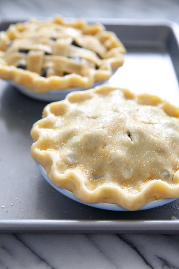 Two unbaked mini blueberrie pies, brushed with egg and sprinkled with turbinado sugar.