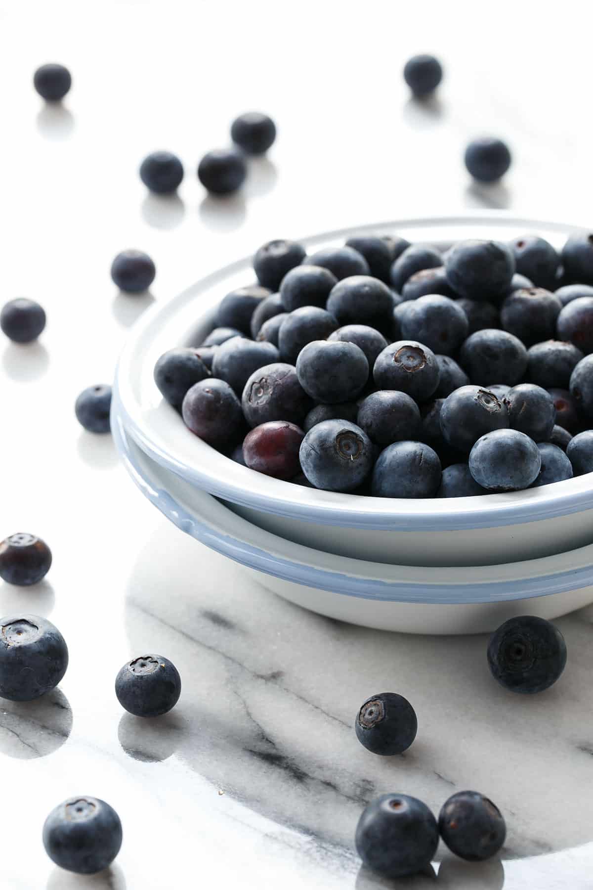 Two mini enamel pie pans filled with fresh blueberries on a marble background.