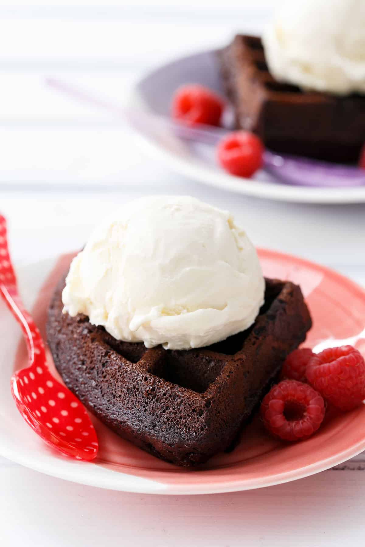 Closeup, one thick chocolate waffle on a colorful red plate, with a scoop of vanilla ice cream on top.