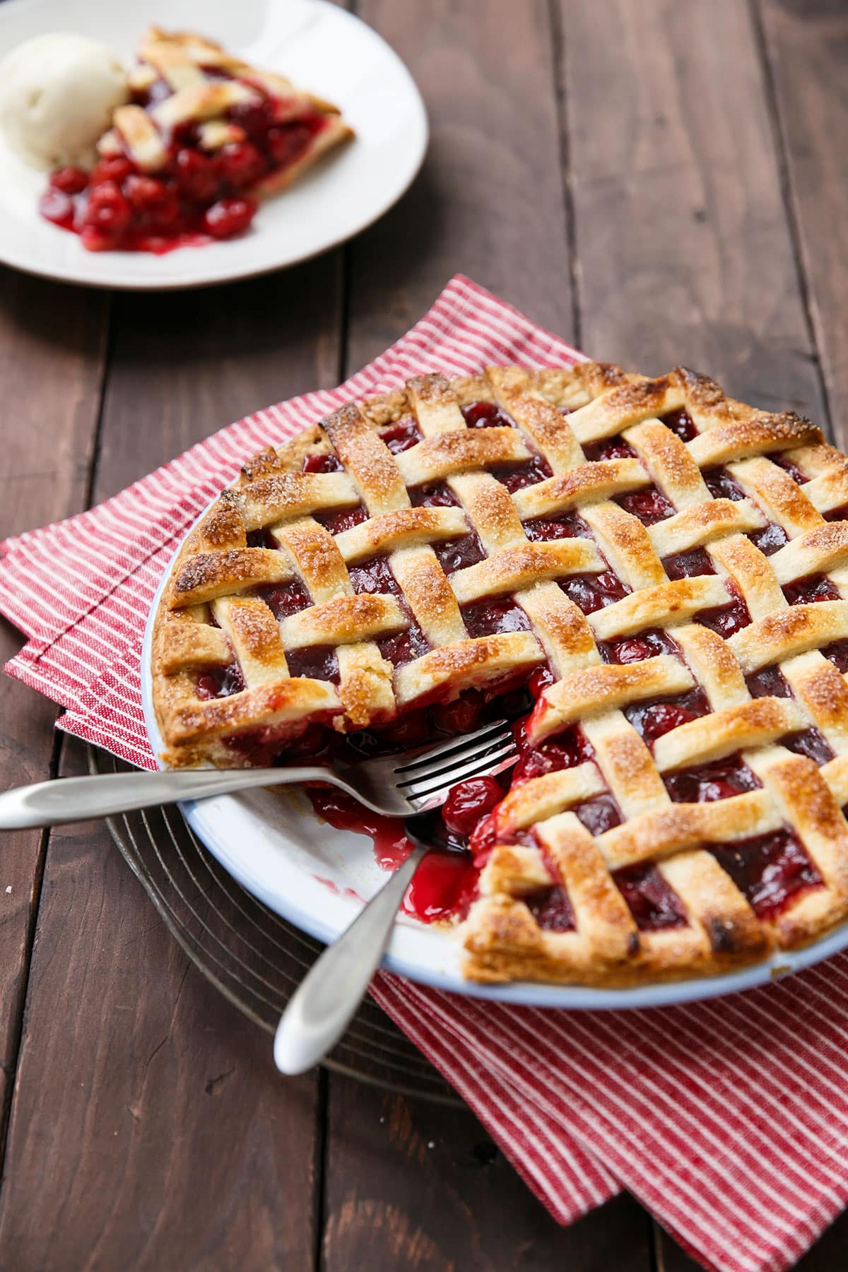 Tart Cherry Pie with a slice cut out in the background, and two forks laying inside the pie pan with the juicy filling.