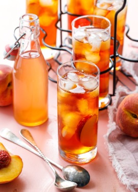 A glass of Cold Brew Peach Iced Tea and a bottle of peach simple syrup in the background