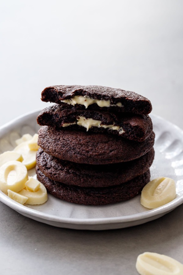 Stack of White Chocolate-Stuffed Chocolate Cookies, top cookie broken in half to show the melted white chocolate center.