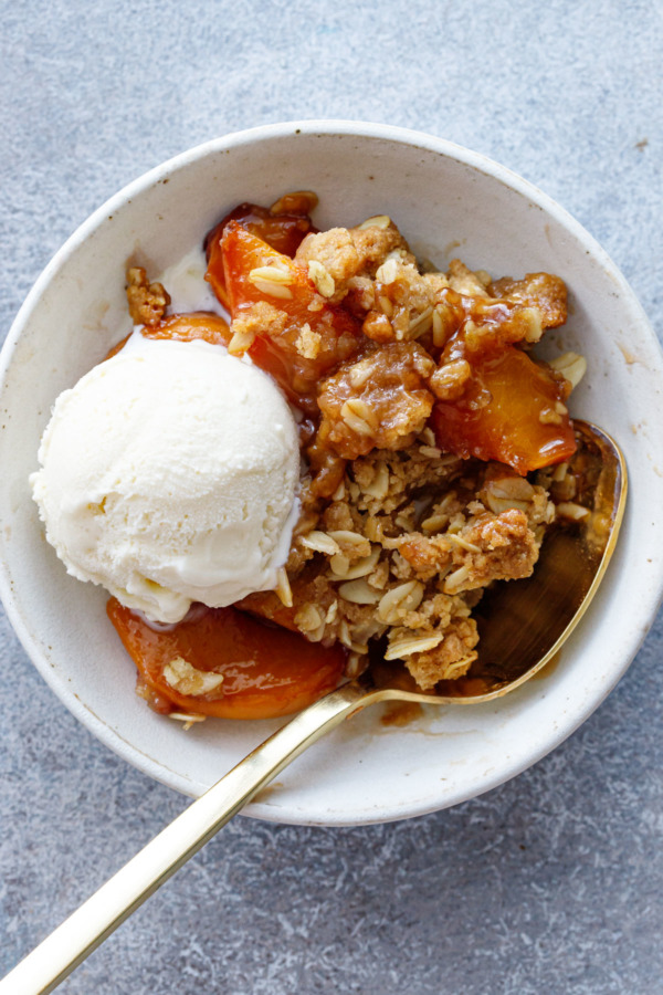 Overhead shot of a small bowl with a scoop of Bourbon Peach Crisp and a scoop of vanilla ice cream with a gold spoon.