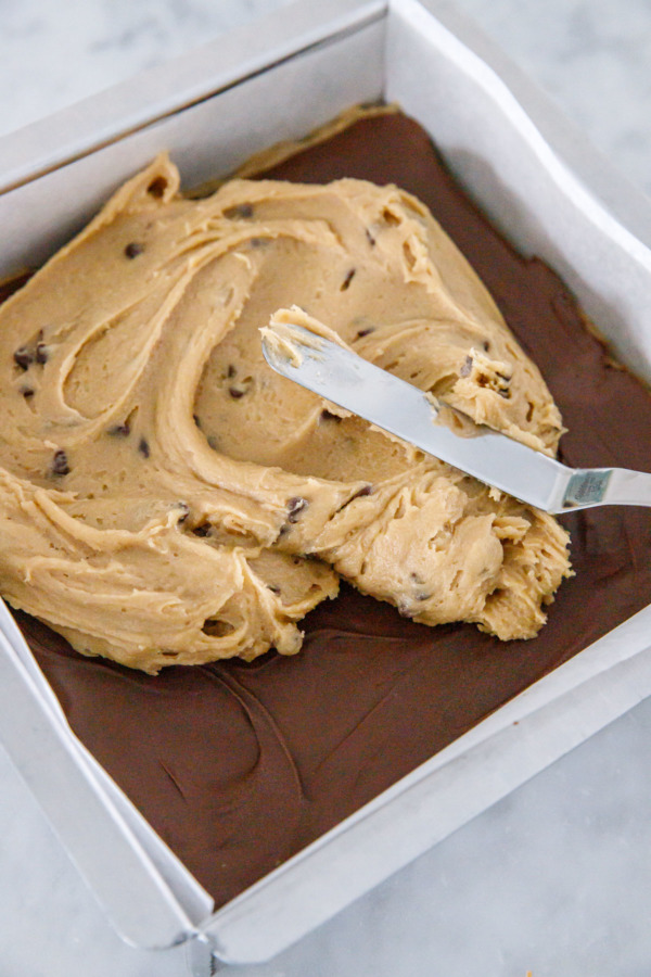 Offset spatula spreading second half of blondie dough on top of nutella.