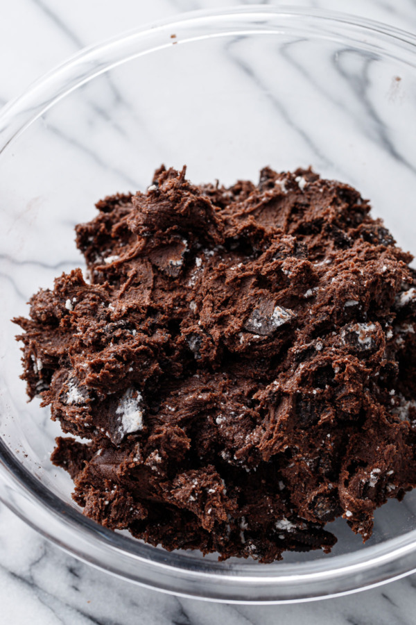 Glass bowl filled with raw chocolate cookie dough mixed with crushed up Oreo chocolate sandwich cookies