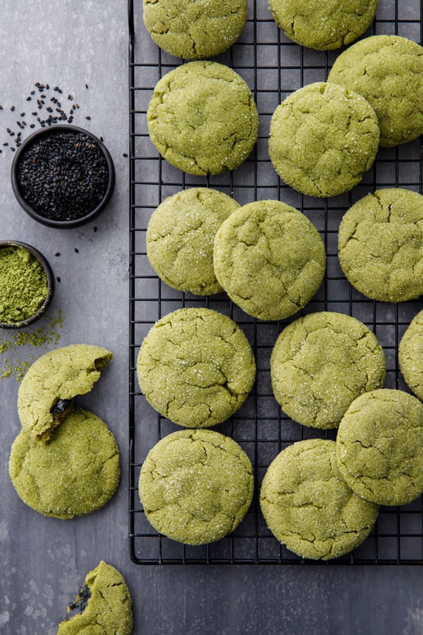 Overhead shot with a cooling rack with rows of matcha sugar cookies, bowls of matcha powder and black sesame seeds.