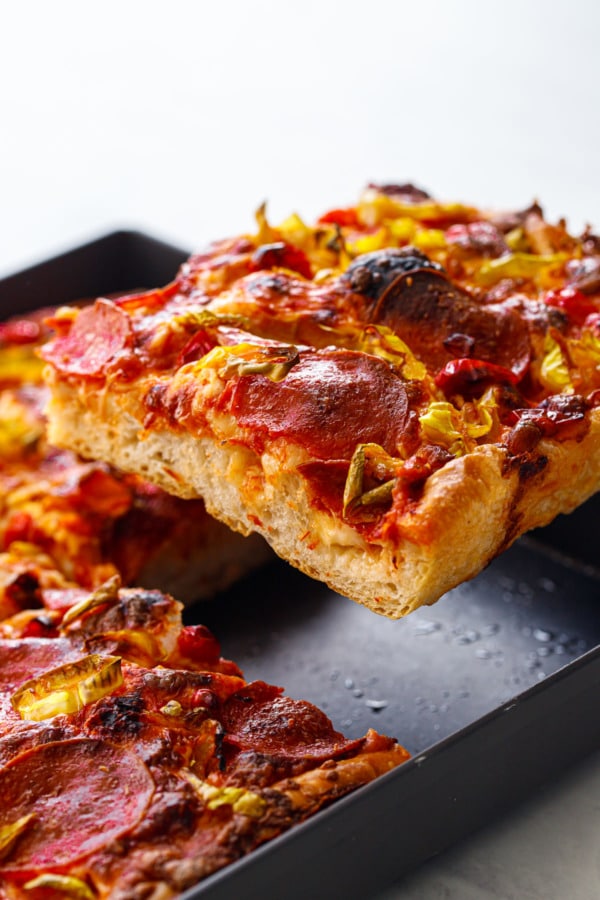 Lifting a slice of pan pizza out of the pan, showing the pockets of melted cheese in the crust.