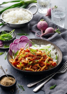 Spicy Korean Egg Roll Bowls with a bowl of rice, pinch bowl of sesame seeds, and whole purple radishes on a dark background.