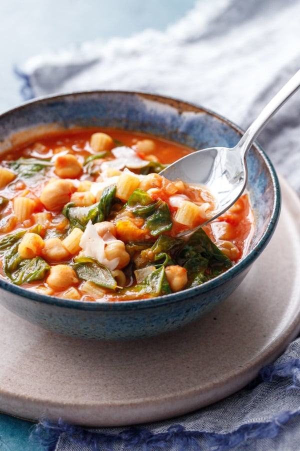 Lifting a spoonful of pasta and chickepea stew from a ceramic bowl