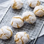 Powdered-sugar coated crinkle cookies on a wire rack, on newsprint parchment on a dark background.