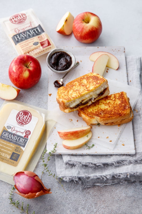Apple butter grilled cheese cut in half on a plate, with raw ingredients around it.