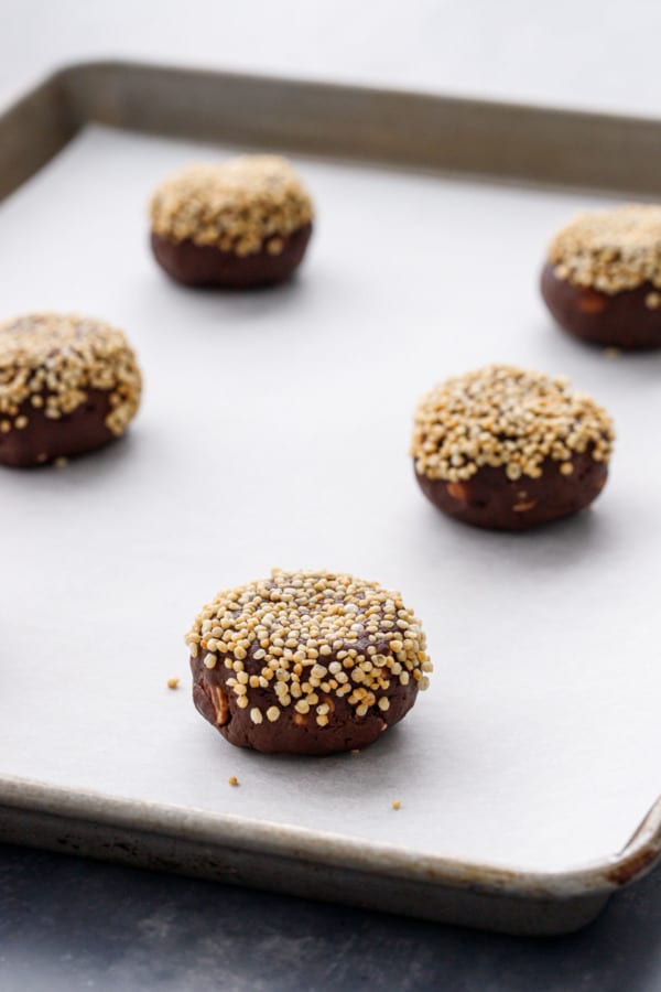 Pucks of cookie dough, tops pressed in puffed quinoa, on a baking sheet