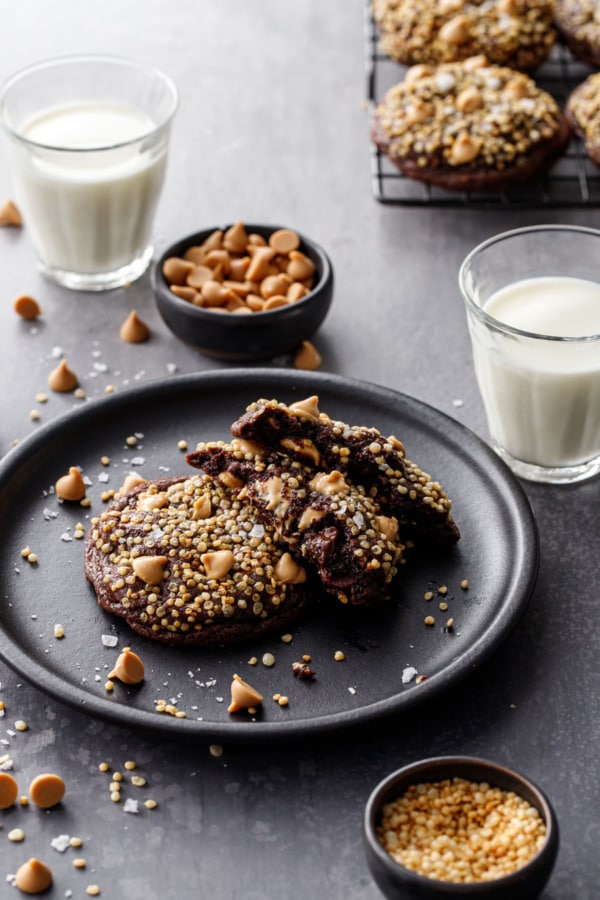 Chocolate cookies topped with puffed quinoa, on a plate with two glasses of milk
