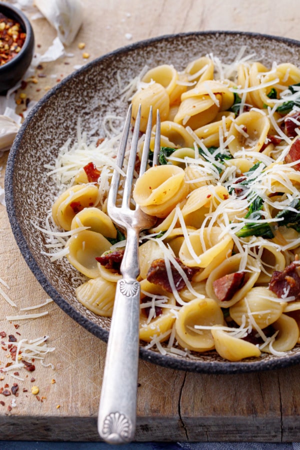 Closeup bowl of orecchiette pasta with vintage silver fork and lots of grated pecorino cheese on top