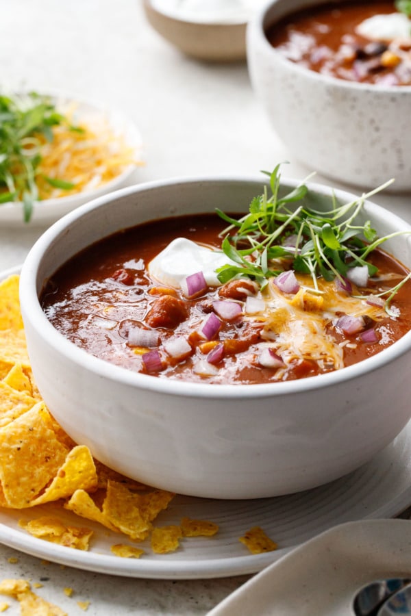 White ceramic bowl with Vegetarian Pumpkin & Three-Bean Chili, tortilla chips on the side