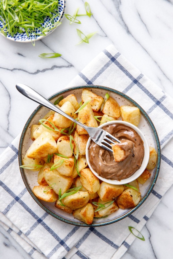 Overhead dish of crispy potatoes with black garlic aioli, sliced green onions on the side