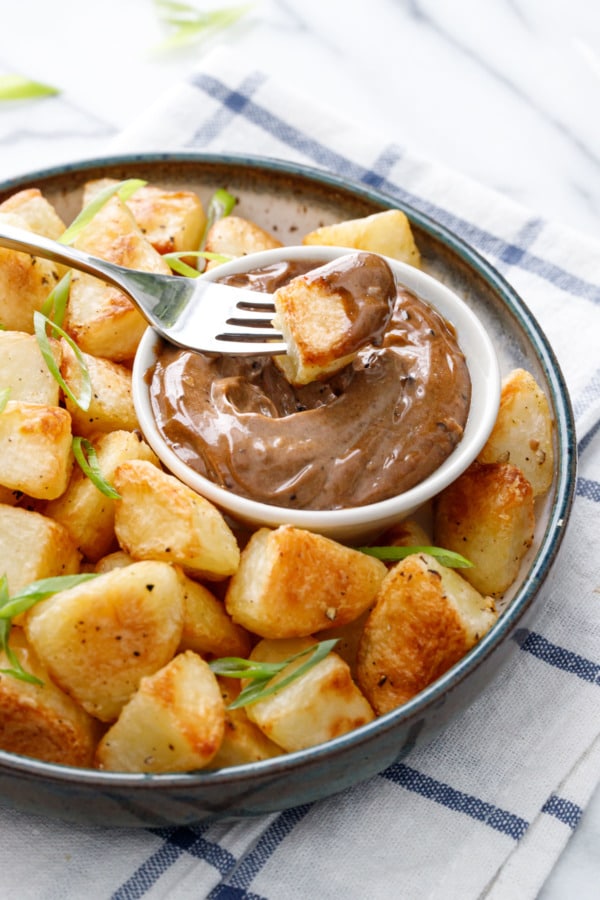 Fork dipping a crispy piece of potato into a dish of black garlic aioli