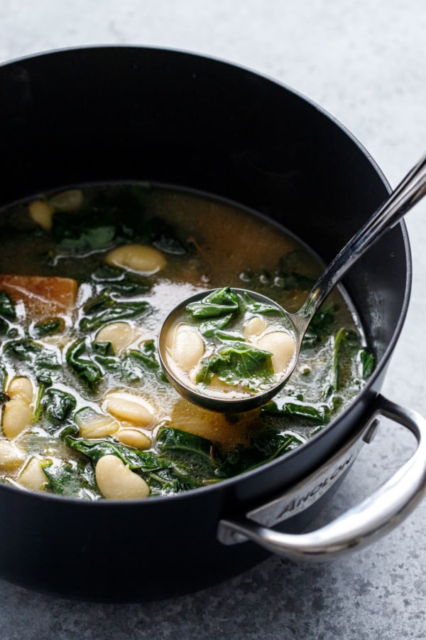 Pot of brothy beans and greens, silver ladle full of beans lifting