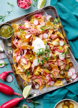 Overhead, sheet pan of Loaded Smoked Chicken Nachos with radishes, micro cilantro on a turquoise background