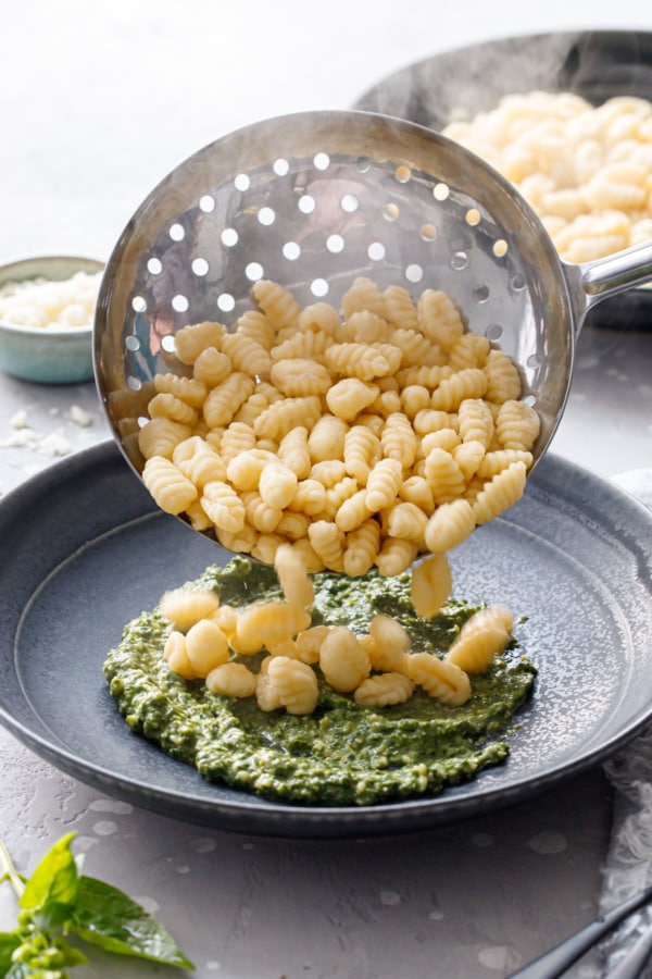 Pouring freshly cooked gnochetti sardi into a black ceramic bowl with swoosh of pesto