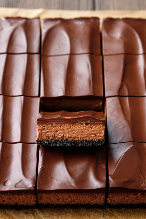 Overhead, cut squares of Chocolate Chai Cheesecake Bars, one propped up to show the layers