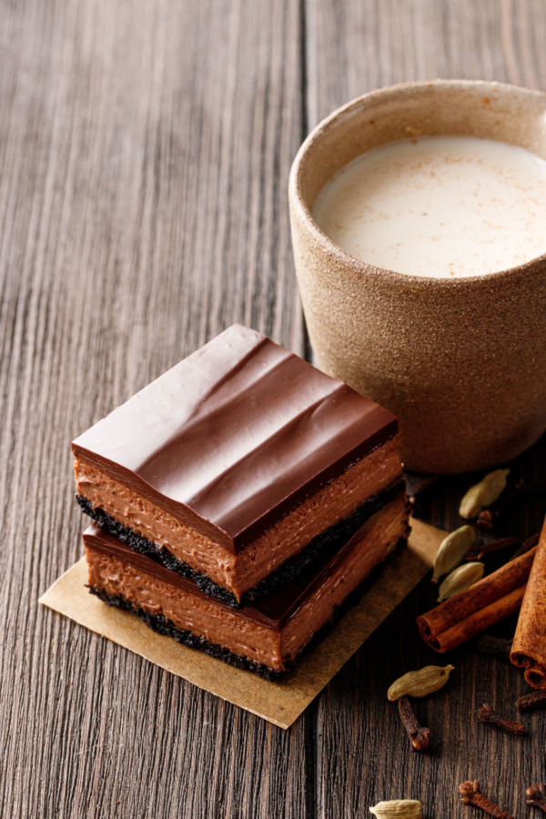 Stack of two Chocolate Chai Cheesecake Bars with a cup of chai and spices