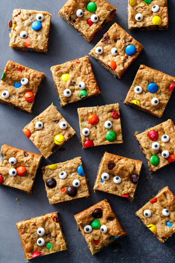 Random arrangement of Monster Cookie Bar squares on black background, with candy eyeballs making faces