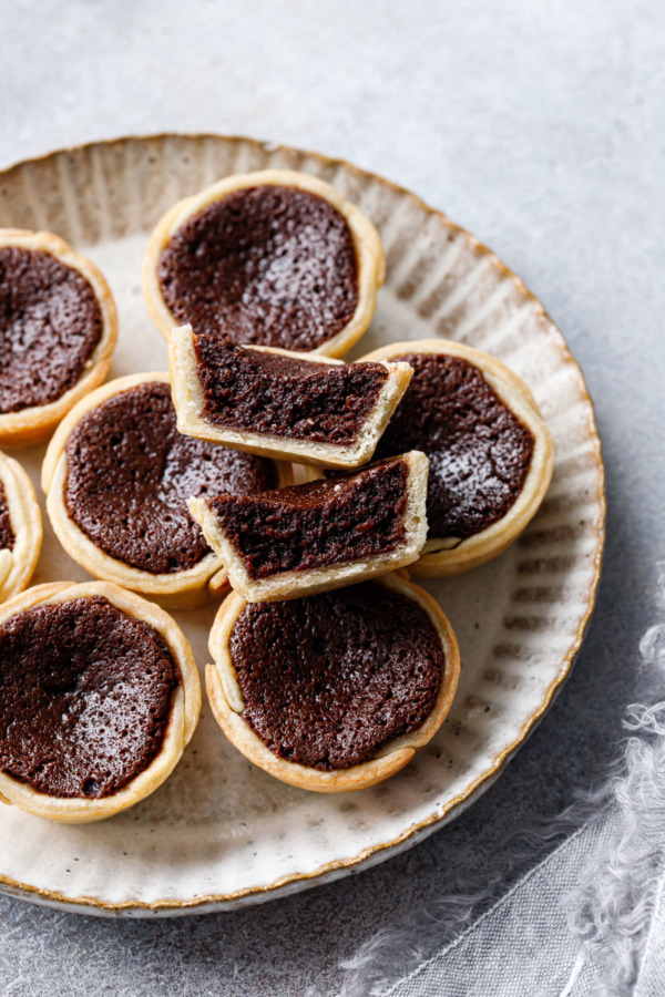 Mini Bourbon Fudge Pies on a ceramic plate, one pie cut in half to show the fudgy texture inside