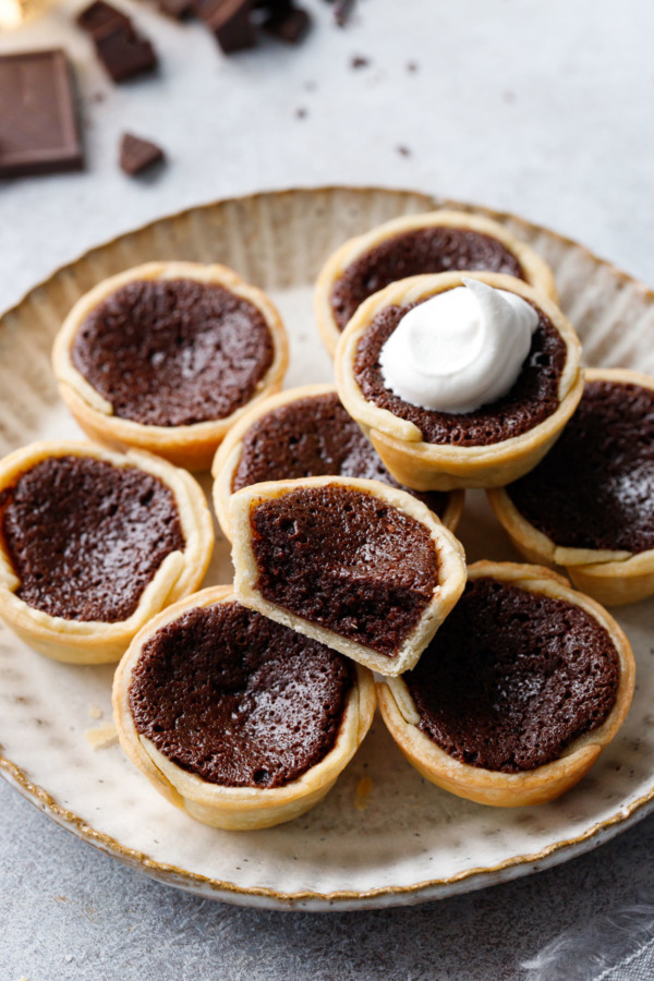 Mini Bourbon Fudge Pies on a ceramic plate, one pie cut in half to show the fudgy texture inside