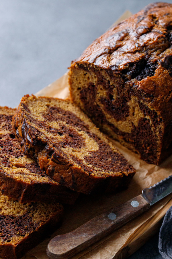 Sliced loaf of Pumpkin Chocolate Swirl Bread on an olivewood bread board with knife
