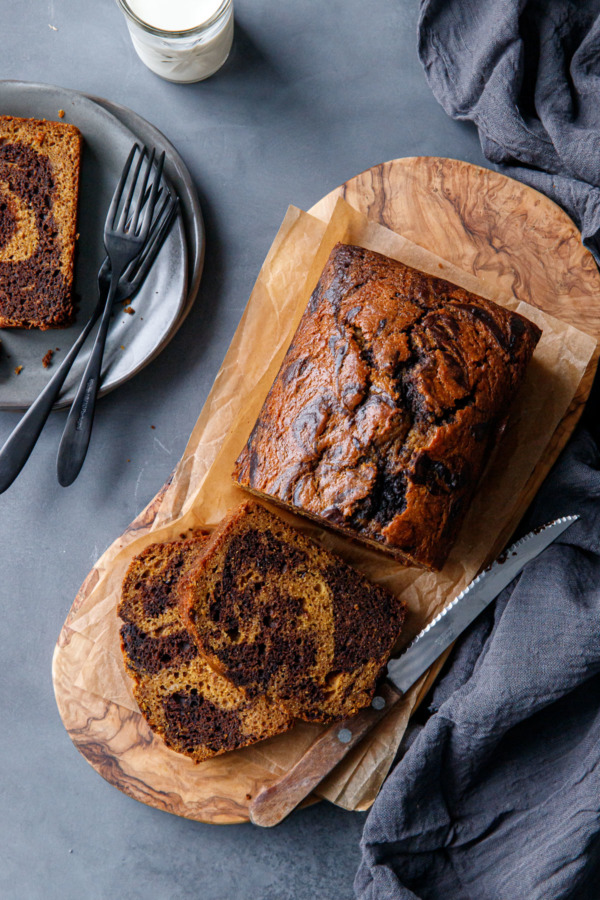 Overhead, Pumpkin Chocolate Swirl Bread, sliced on a wood board with a slice on a plate and a glass of milk