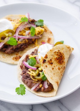 Two Easy Refried Black Bean Tacos on a white plate, topped with fresh cilantro