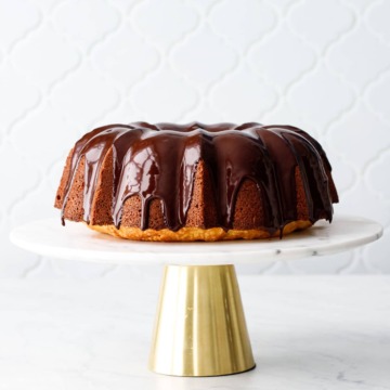 Almond Bundt Cake with Amaretto Ganache on a gold and marble cake stand with tile background