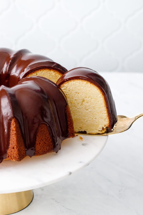 One slice of Almond Bundt Cake with Amaretto Ganache being pulled out with a gold cake server.