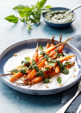Blue and white ceramic platter with pile of Roasted Carrots, drizzled with Basil and Carrot Top Pesto on a blue background.