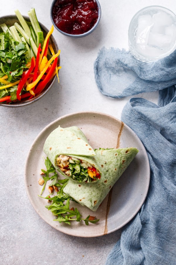Overhead, plate with Curried Chicken, Chickpea & Arugula Wrap cut in half diagonally, plus bowl of veggies and smaller one of cranberry sauce.