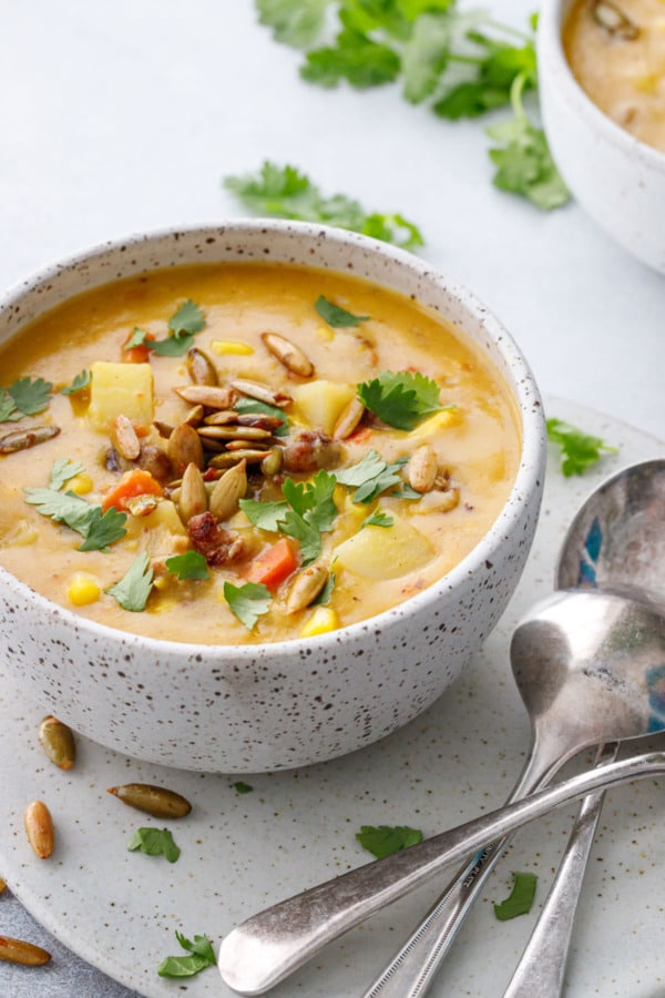 Sausage & Corn Chowder in a speckled ceramic bowl, silver spoons and scattered cilantro leaves.