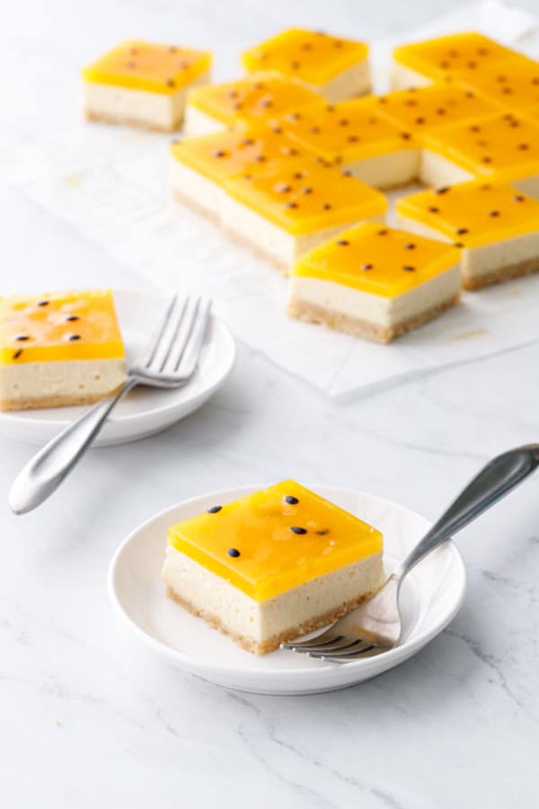 Small white plate with square of Passionfruit Cheesecake, silver fork, and more cut bars in the background.